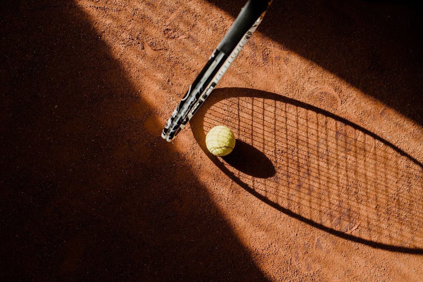 Tennis ball and racket shadow on a red clay court (illustrative photo by cottonbro studio on Pexels, not Spectrum Center)