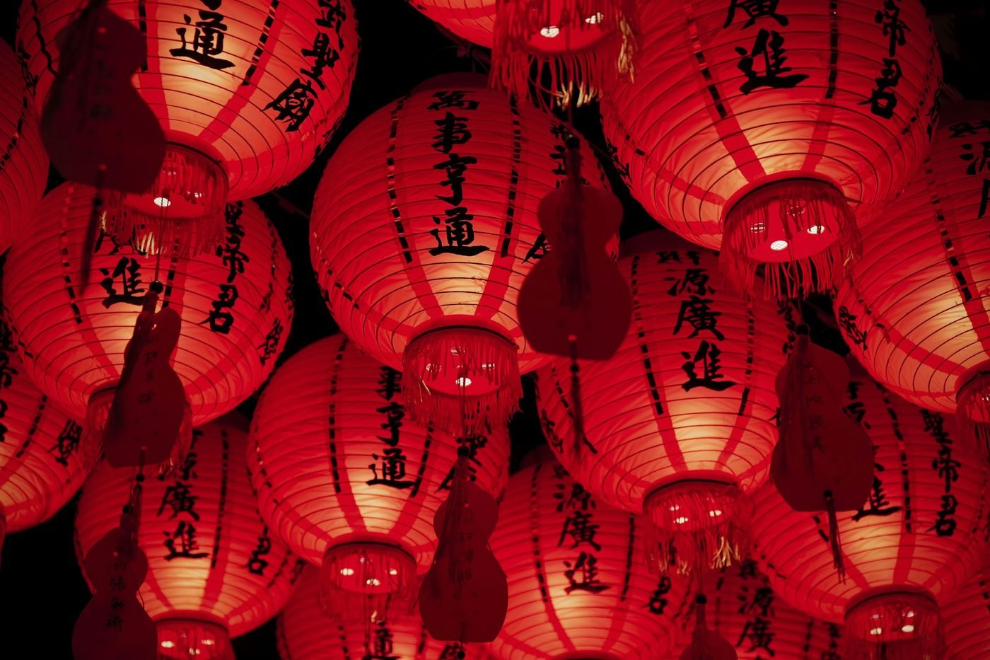 Red paper lanterns with Chinese characters glowing against a dark background (illustrative photo by H&CO on Unsplash, not a festival display)