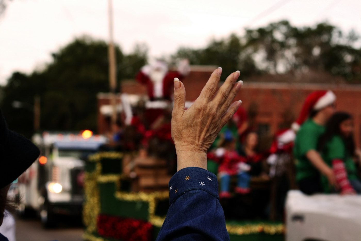 A raised hand in front of a Christmas parade float carrying Santa and helpers (illustrative photo by ana G. Pascual on Unsplash, not the Raleigh parade)